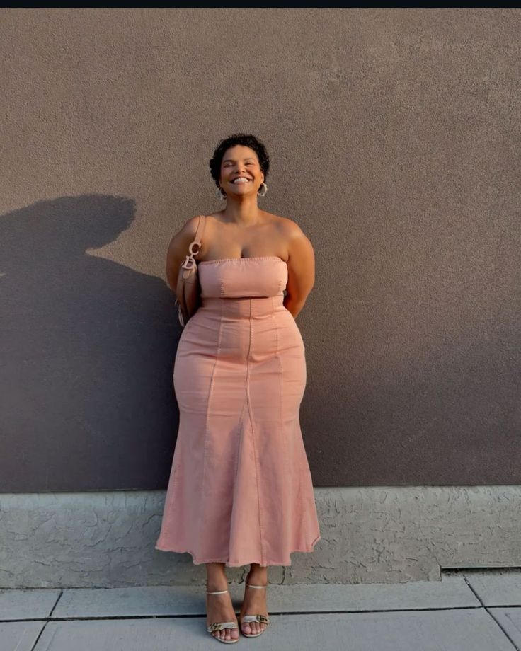 Woman in a pink strapless dress and high heels smiling outdoors