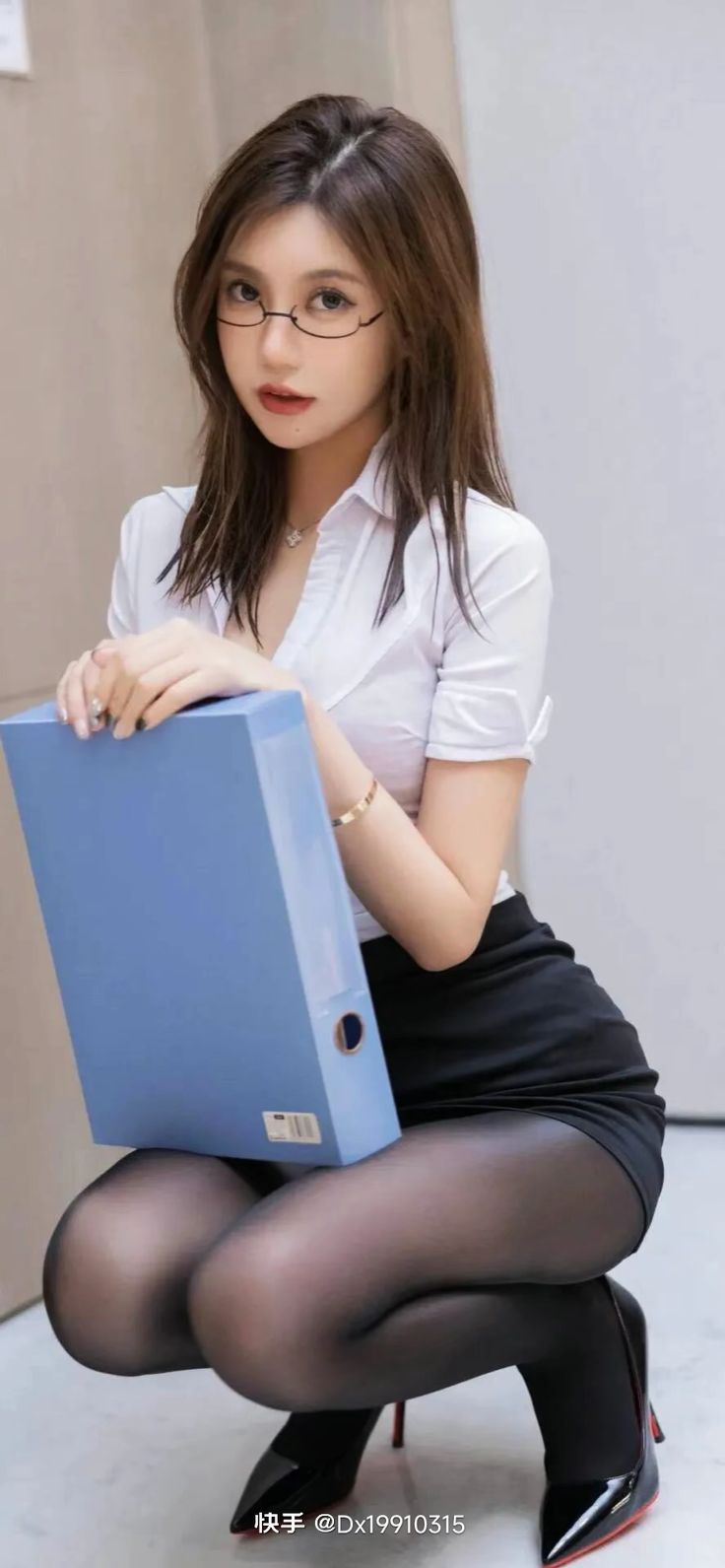 Woman in a white shirt and black skirt with pantyhose holding a blue binder