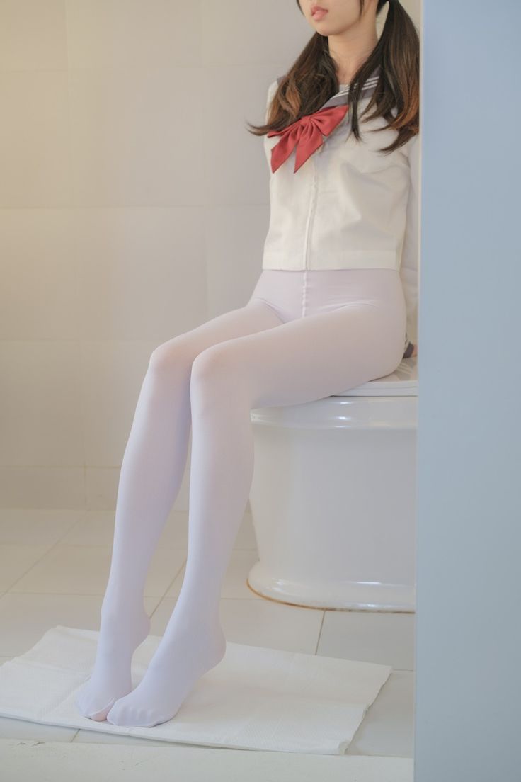 Person in a school uniform with white tights and pigtails sitting indoors