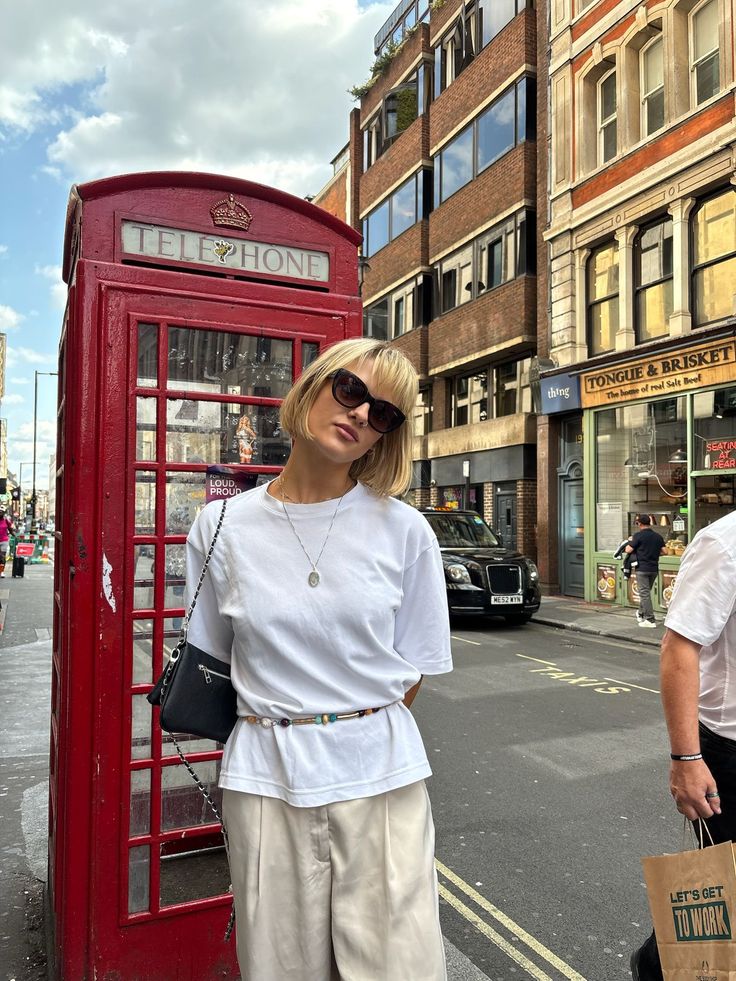 Woman with short blonde hair and sunglasses standing next to a red telephone booth