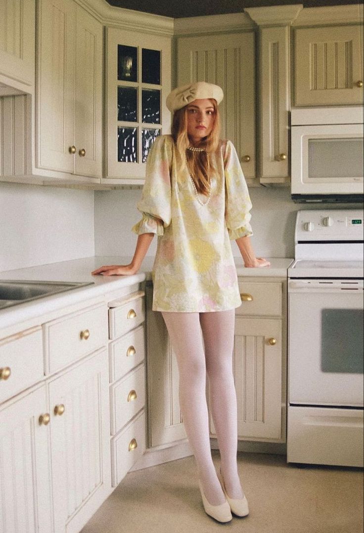 Woman in a floral dress, beret, and white tights standing in a kitchen