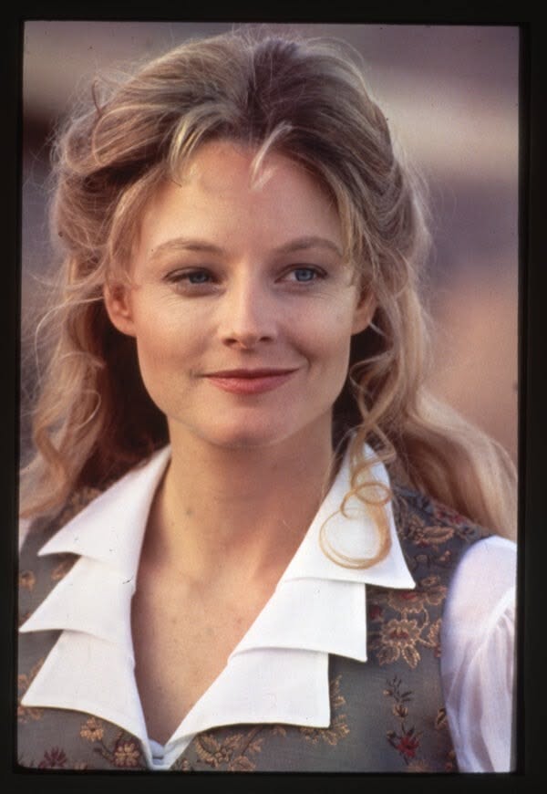 Woman with blonde hair and blue eyes wearing a white shirt and patterned vest
