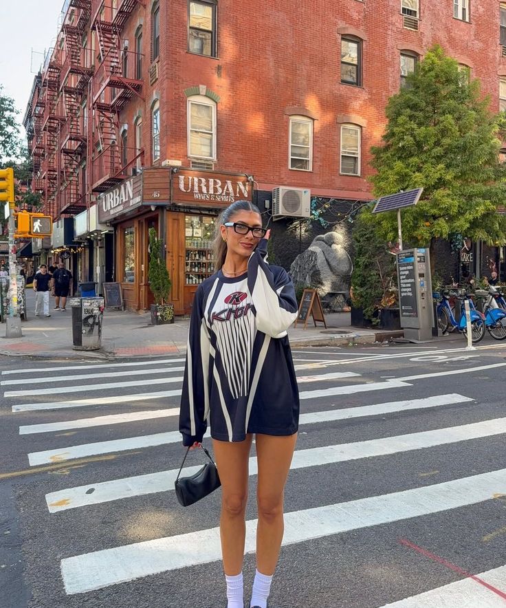Woman in an oversized shirt and glasses standing on a city street