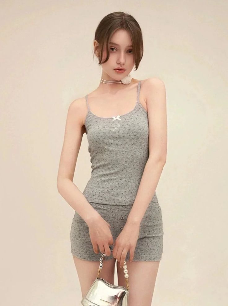 Woman in a gray camisole and shorts holding a silver handbag