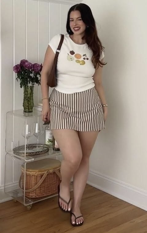 Woman with long dark hair wearing a striped skirt and white t-shirt indoors