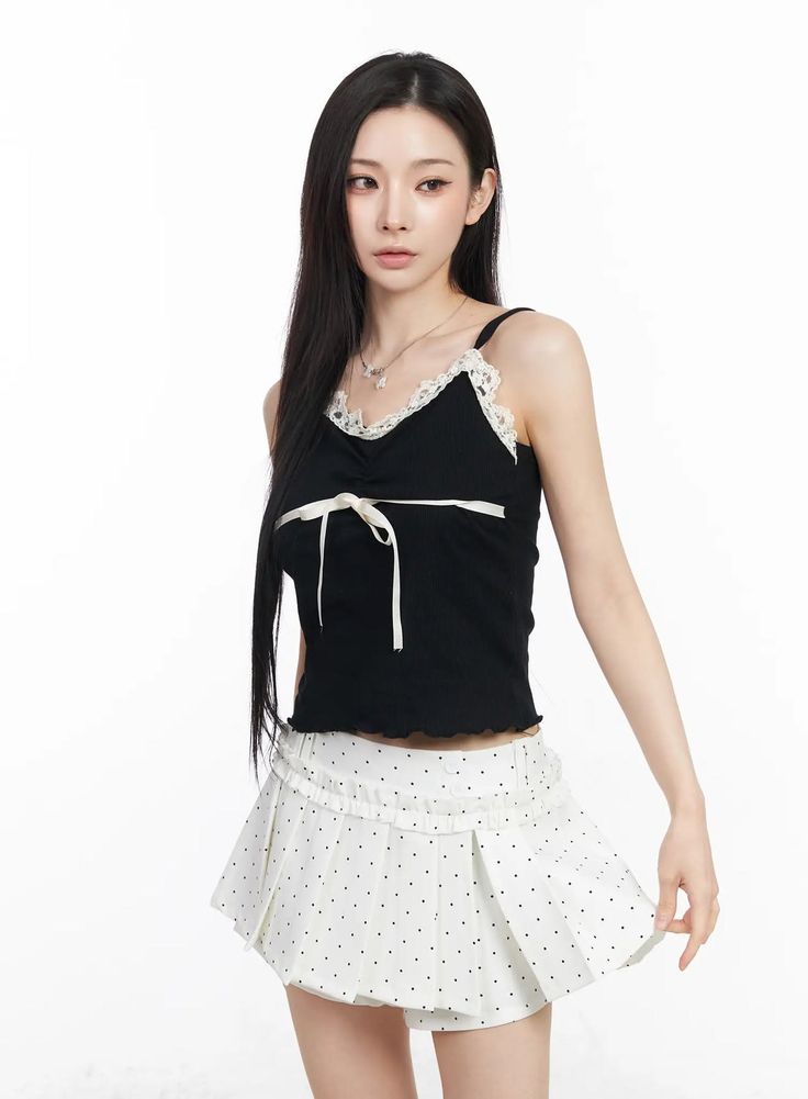 Woman with long black hair wearing a black top and white polka dot skirt