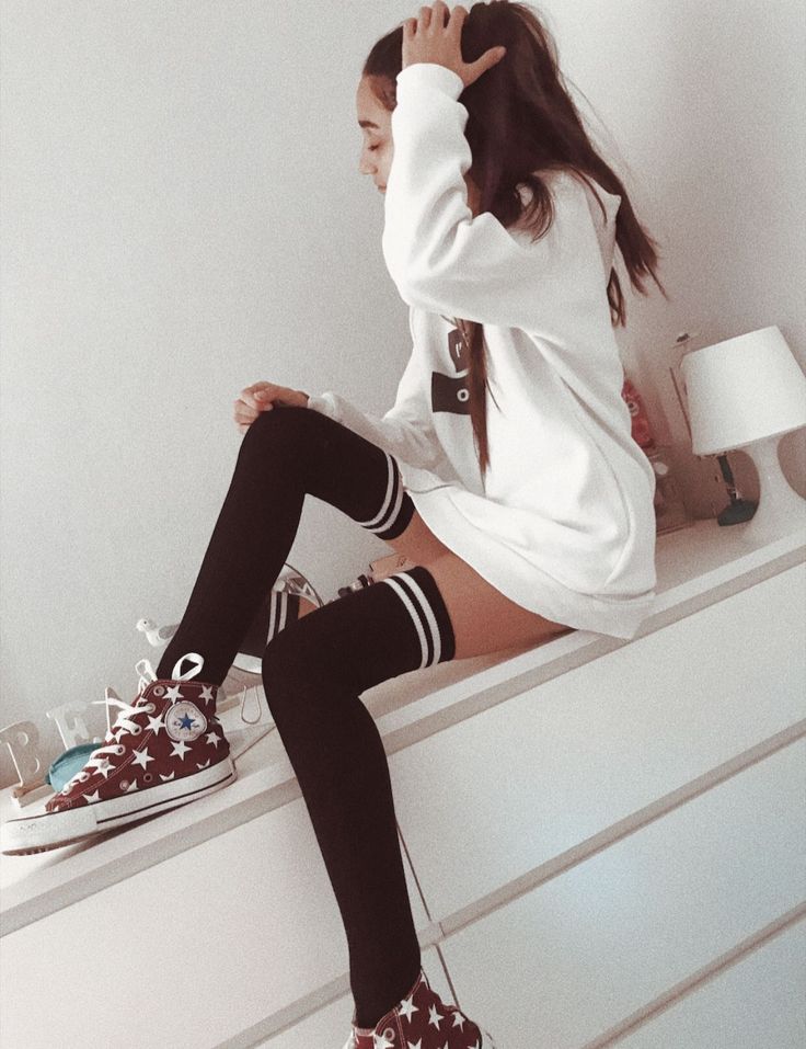 Person in a white hoodie and thigh-high socks sitting on a dresser