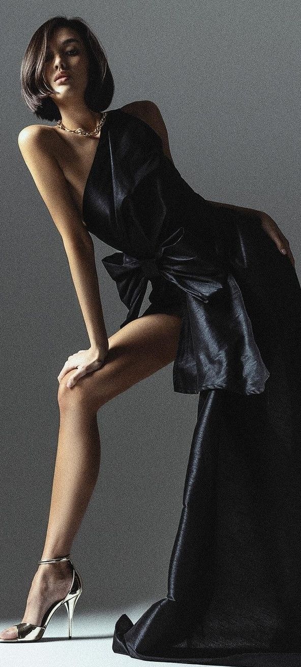 Woman in a black dress and gold necklace posing in a studio