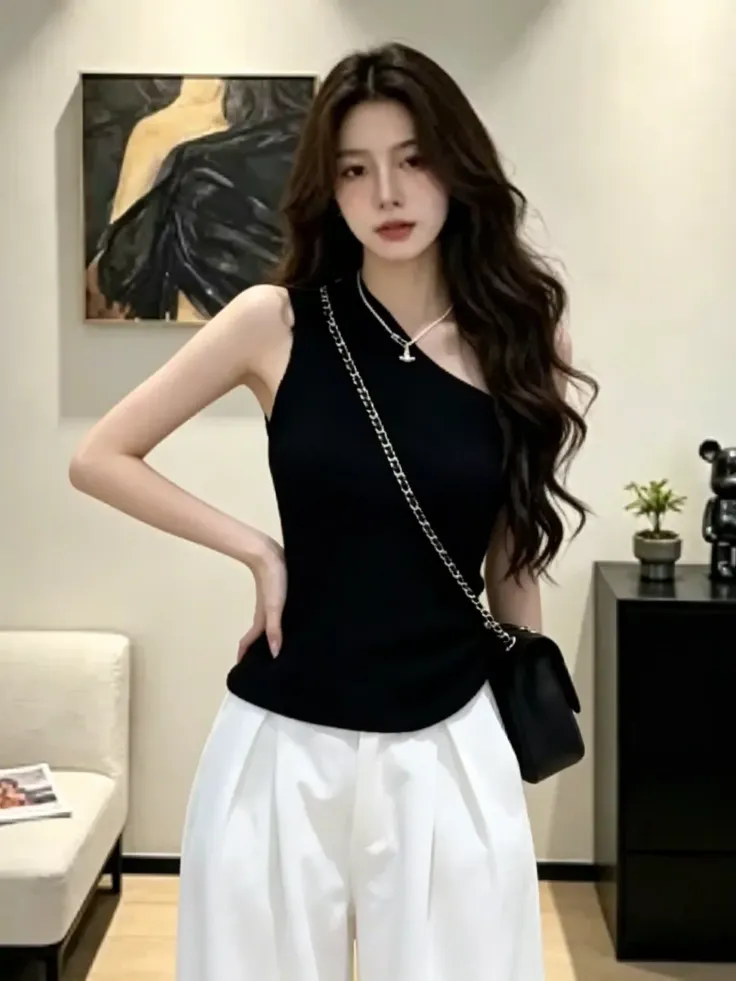 Woman with long dark hair wearing a black one-shoulder top and white pants indoors