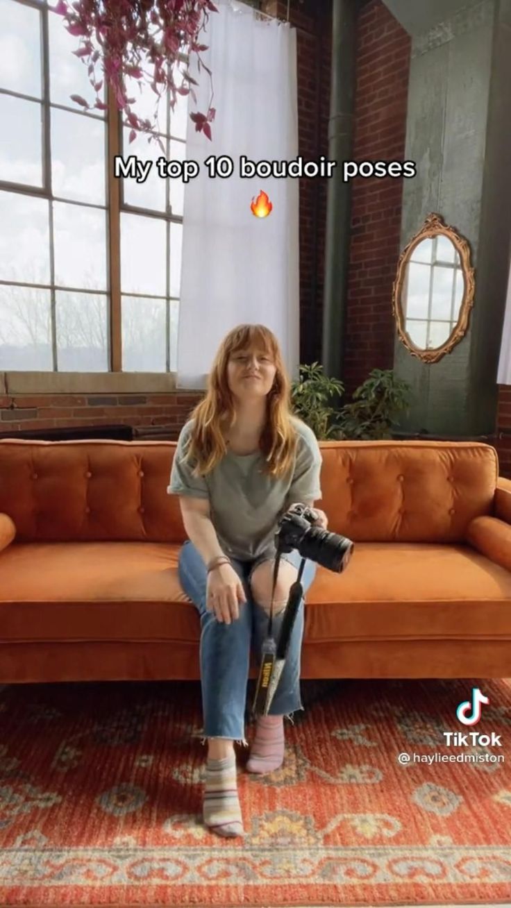 Woman with a camera sitting on an orange couch in an indoor setting