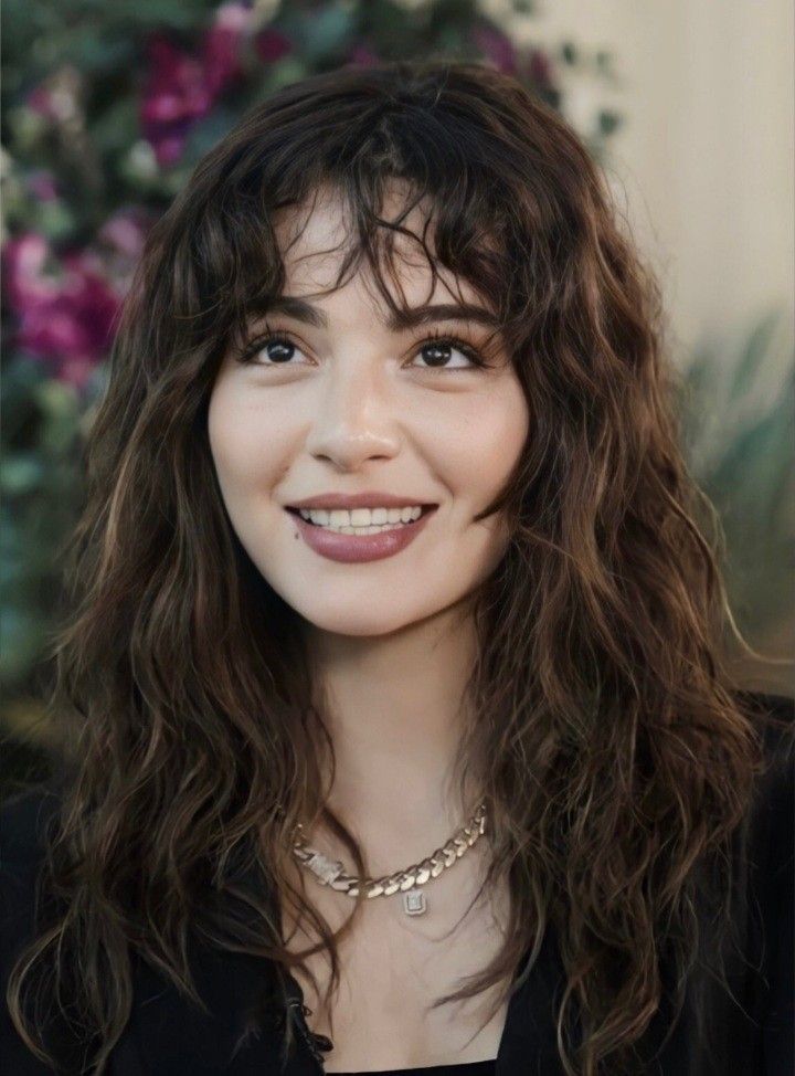 Woman with long wavy hair and bangs smiling outdoors