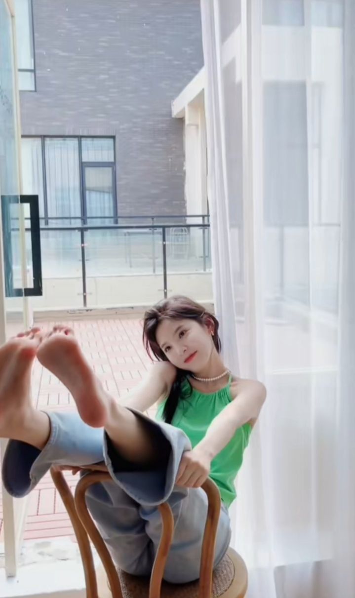 Woman in a green top and jeans posing indoors with bare feet up