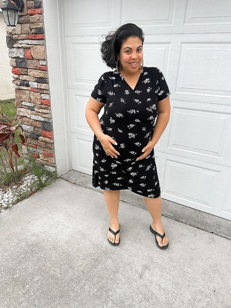 Woman in a black floral dress and flip flops standing outdoors
