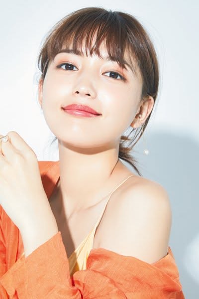 Woman with short hair and bangs wearing an orange shirt and pearl earrings
