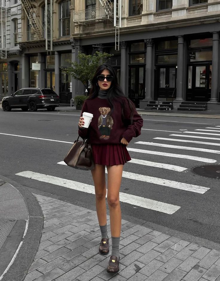 Woman in a sweater and pleated skirt holding a coffee cup on a city street