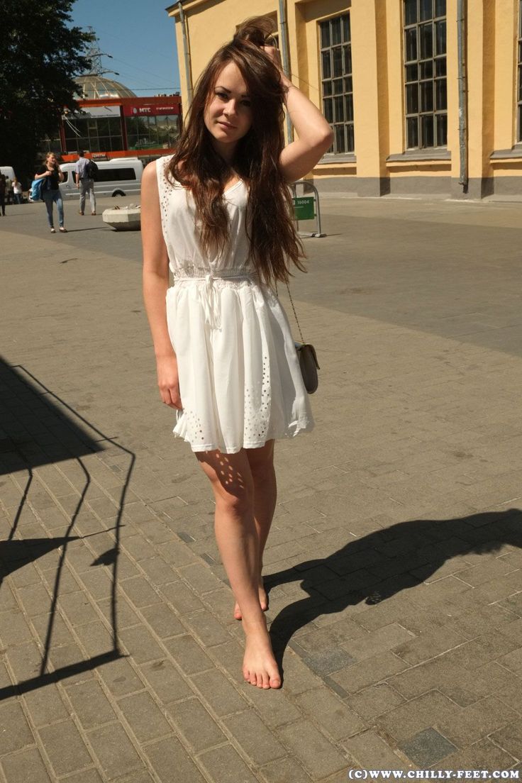 Young woman in a white dress standing barefoot on a paved street