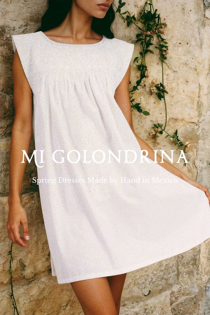 Woman in a white dress standing against a stone wall with vines