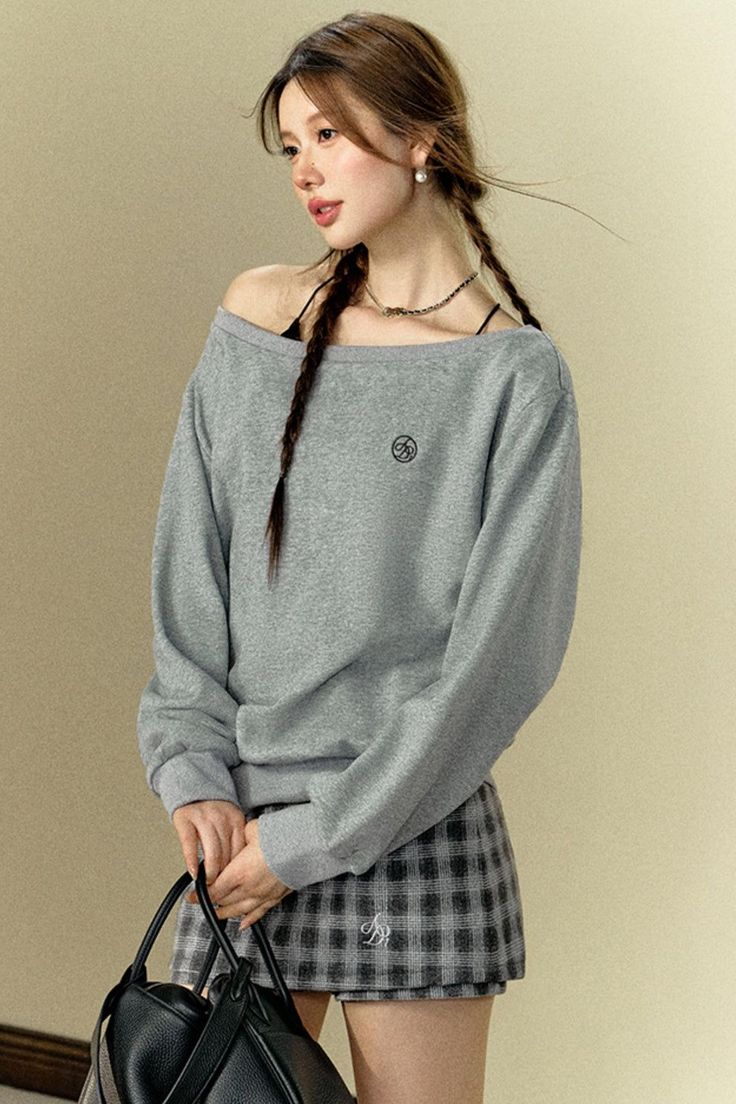 Woman with braids wearing an off-shoulder top and plaid skirt, holding a black handbag