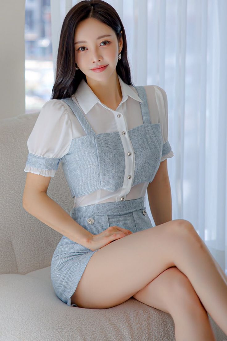 Woman with long dark hair wearing a light blue skirt and white shirt, sitting indoors