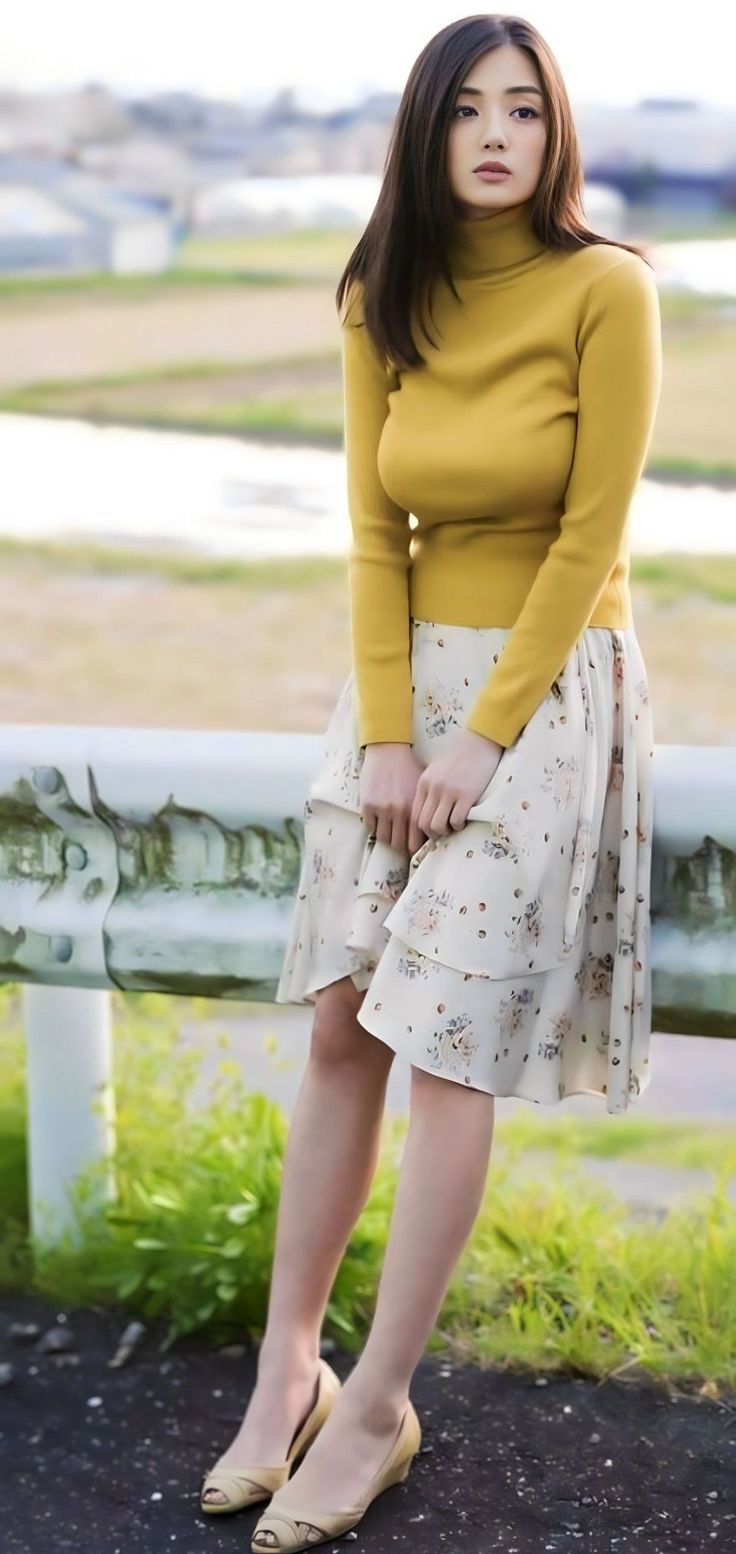 Woman in a yellow turtleneck and floral skirt leaning on a guardrail outdoors