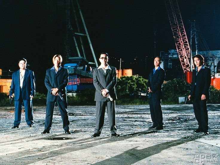 Five men in suits holding guns at night in an outdoor industrial area