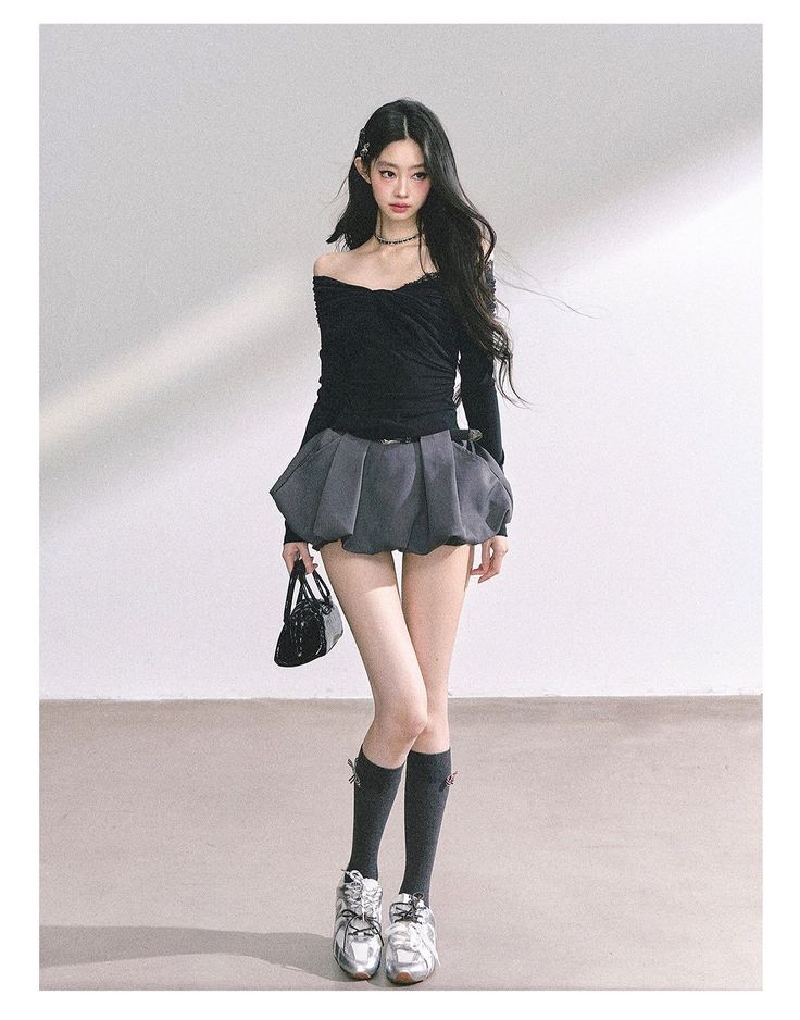 Woman with long dark hair wearing an off-shoulder top and mini skirt in a studio