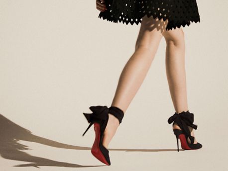 Woman's legs in black high heels with red soles and bows, wearing a black dress