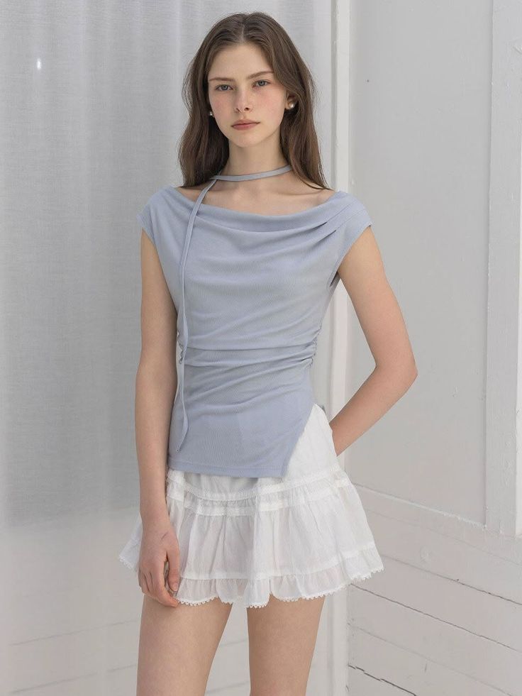 Woman with long hair wearing a light blue top and white mini skirt indoors