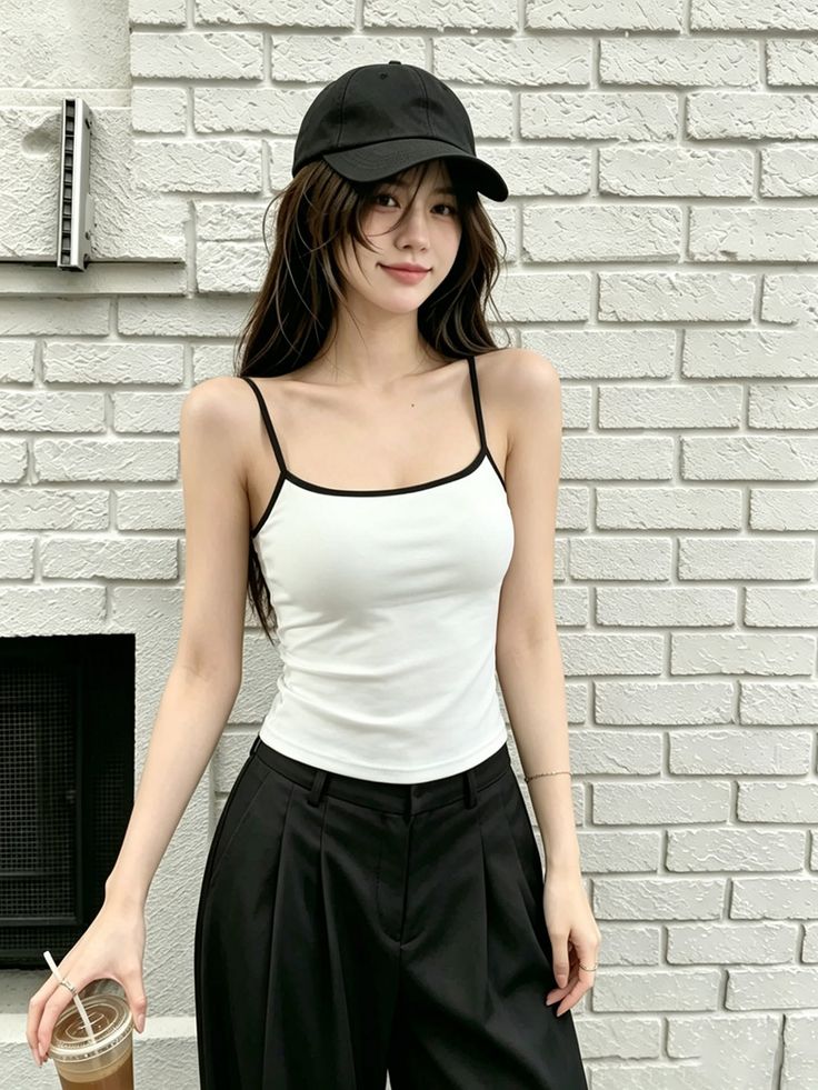 Woman in a white camisole and black cap standing against a brick wall