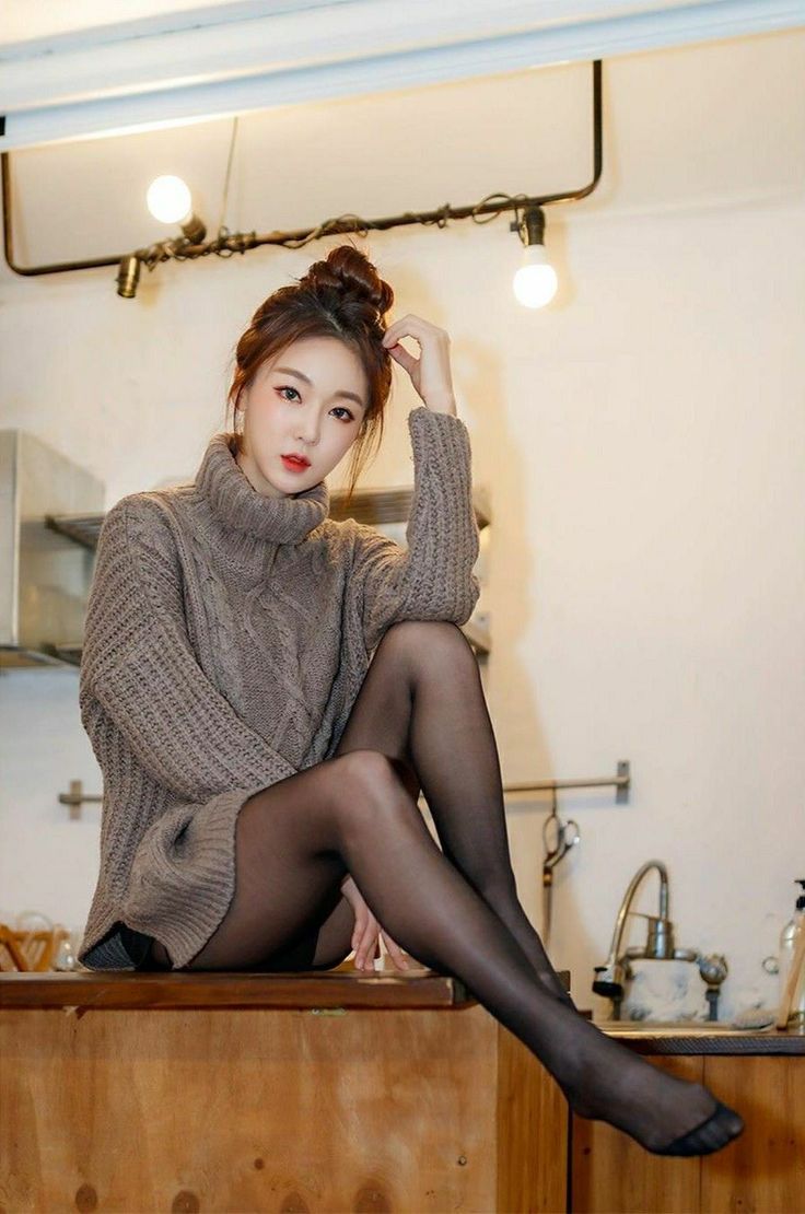 Woman in a turtleneck sweater and black pantyhose sitting indoors