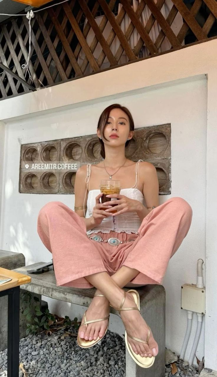 Woman in a white top and pink pants sitting outdoors with a drink
