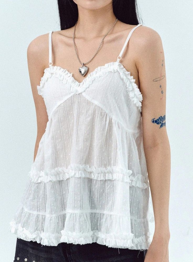 Woman in a white ruffled top with a heart locket and visible tattoos
