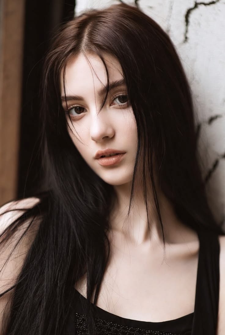 Woman with long dark hair wearing a black top, looking directly at the viewer