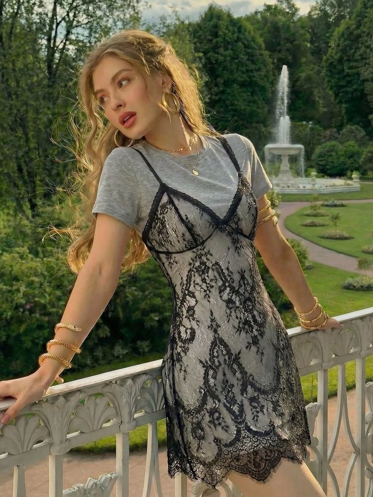 Woman in a lace dress and gold jewelry in a garden with a fountain