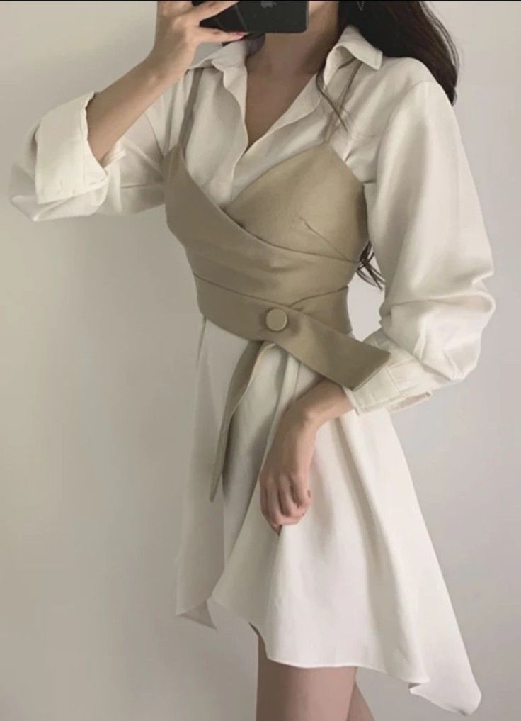 Woman in a white shirt dress with a beige corset top, holding a phone
