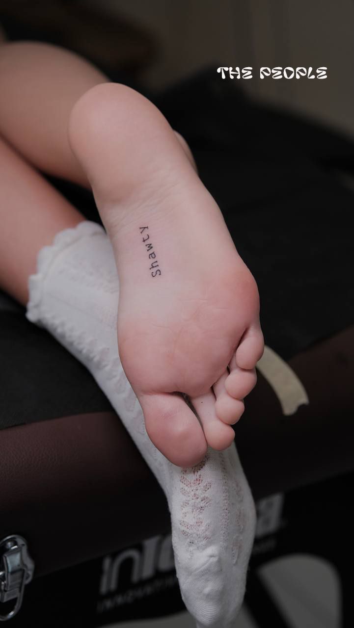 Close up of a foot with a 'Shawty' tattoo on the sole, wearing a white sock