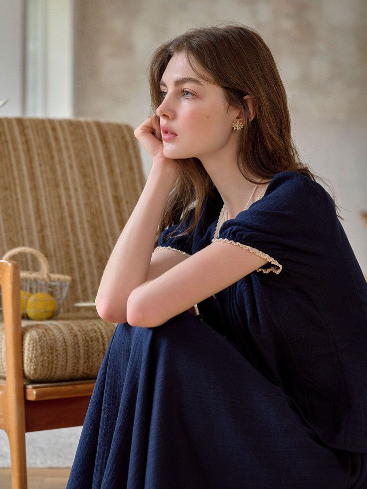 Woman in a navy blue dress with lace trim, sitting indoors