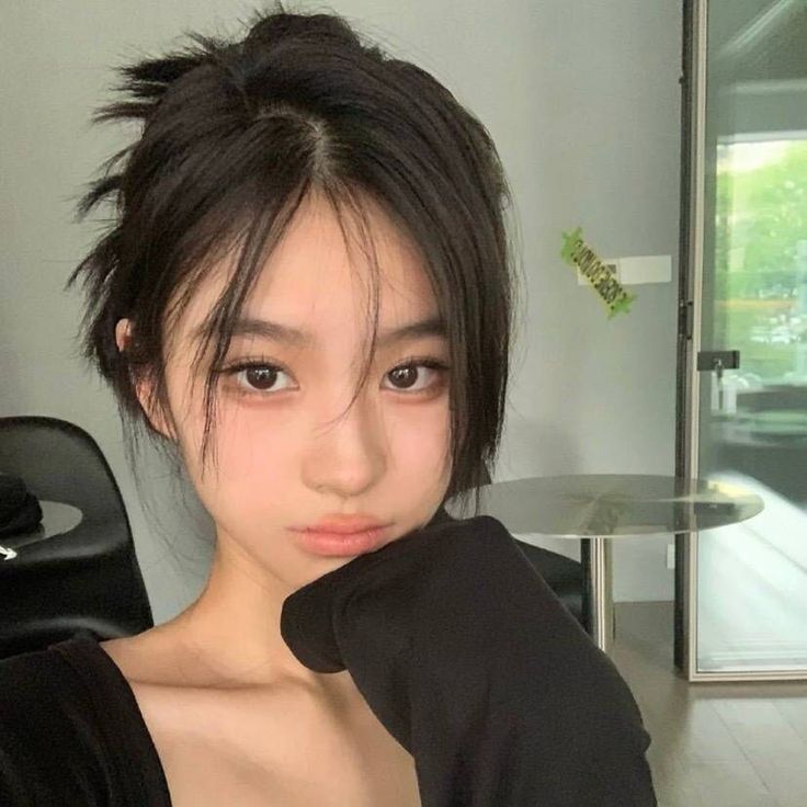 Woman with black hair in a messy bun wearing a black top indoors