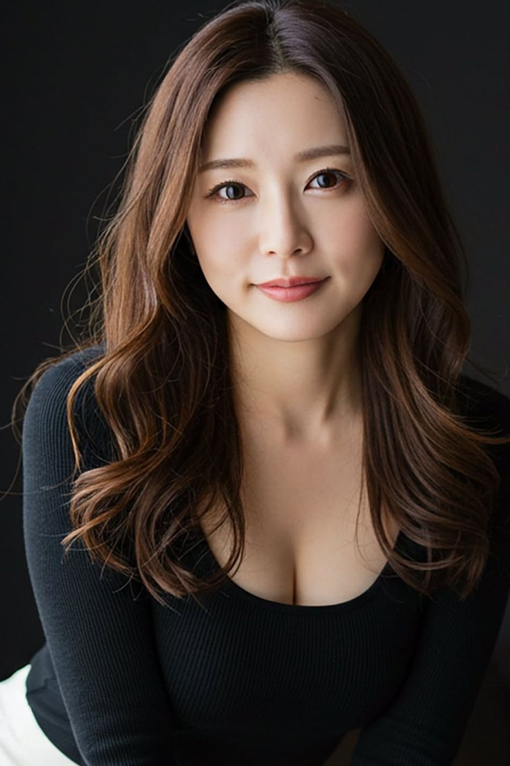 Woman with long brown hair wearing a black top with visible cleavage