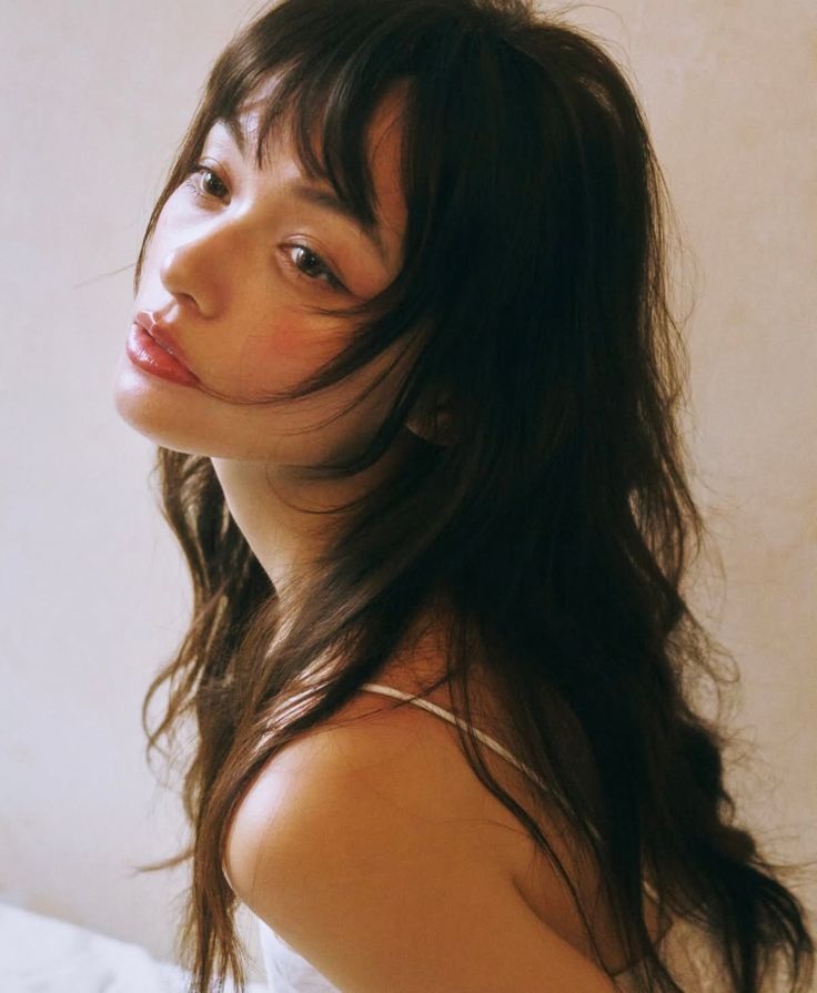 Woman with long dark hair and thin strap top looking over her shoulder