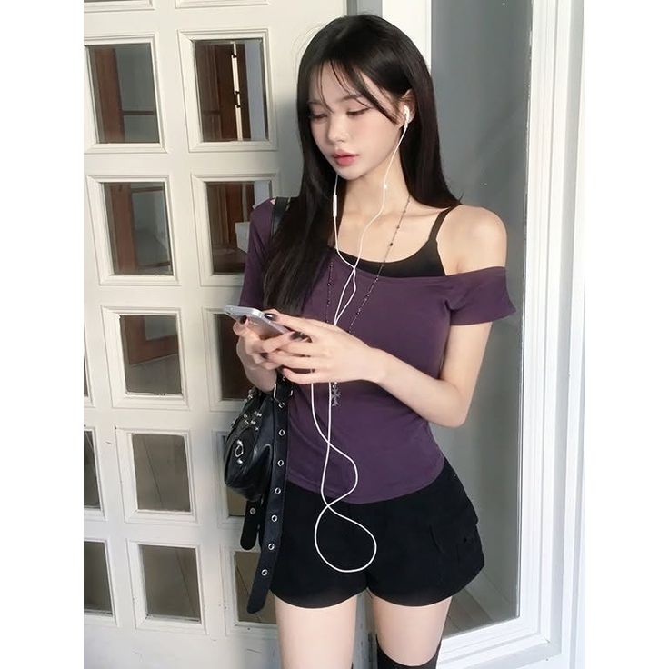 Woman with long black hair wearing an off-shoulder top and shorts, looking at her phone