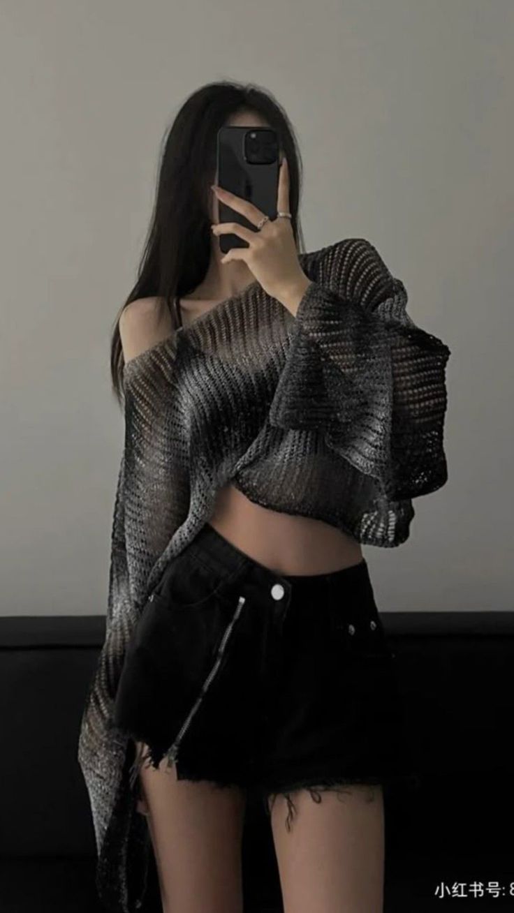 Woman with long black hair taking a mirror selfie in a crop top and shorts