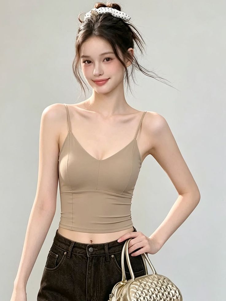 Woman in a spaghetti strap top and dark jeans holding a gold handbag