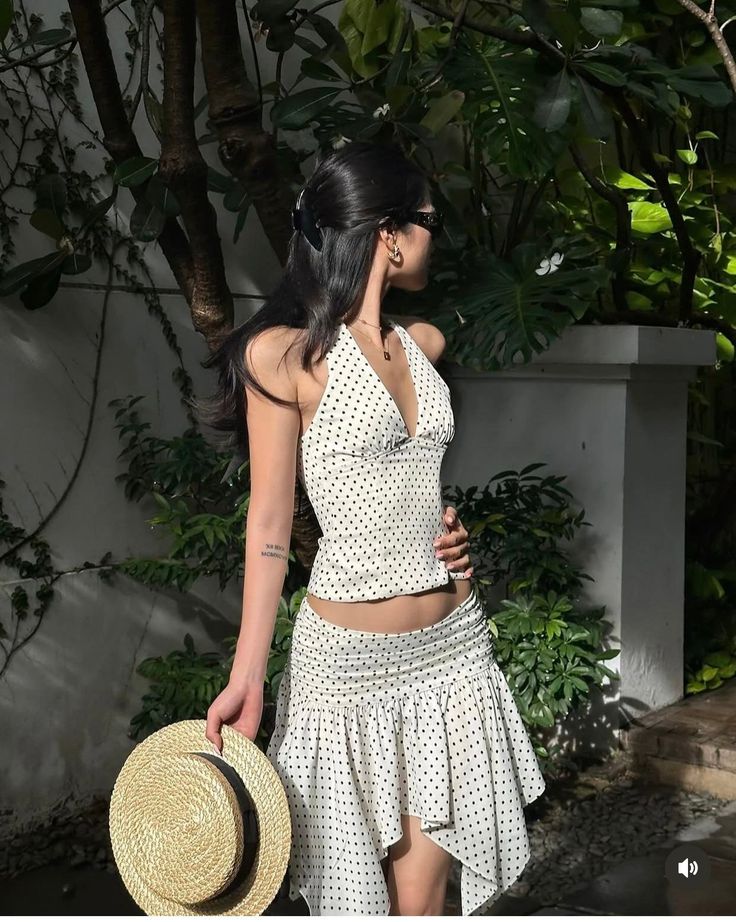 Woman in a white polka dot halter top and mini skirt holding a straw hat outdoors