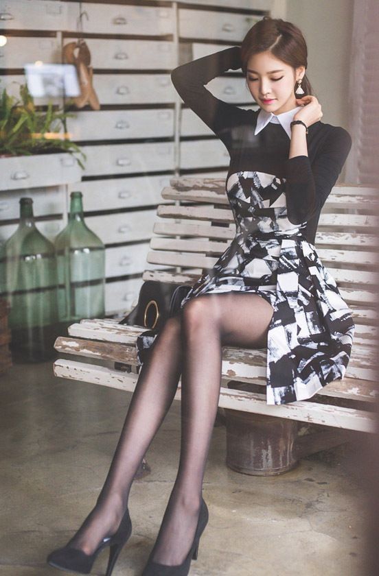 Woman in a black and white dress and pantyhose sitting on a bench indoors