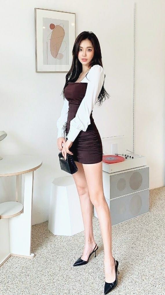 Woman in a brown mini dress and white long-sleeve top holding a black handbag