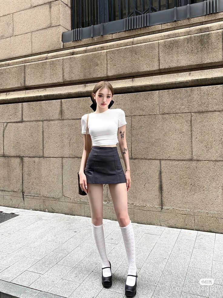Woman in a white crop top and black mini skirt with knee high socks outdoors
