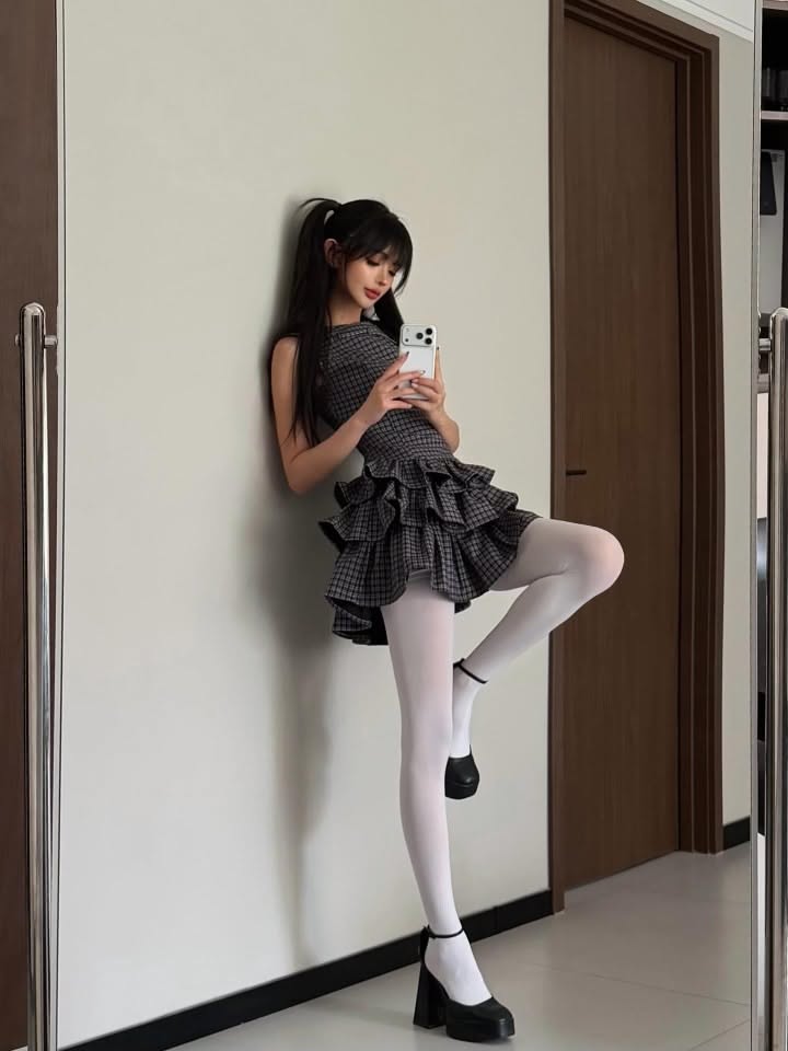 Woman in a plaid dress and white tights taking a mirror selfie