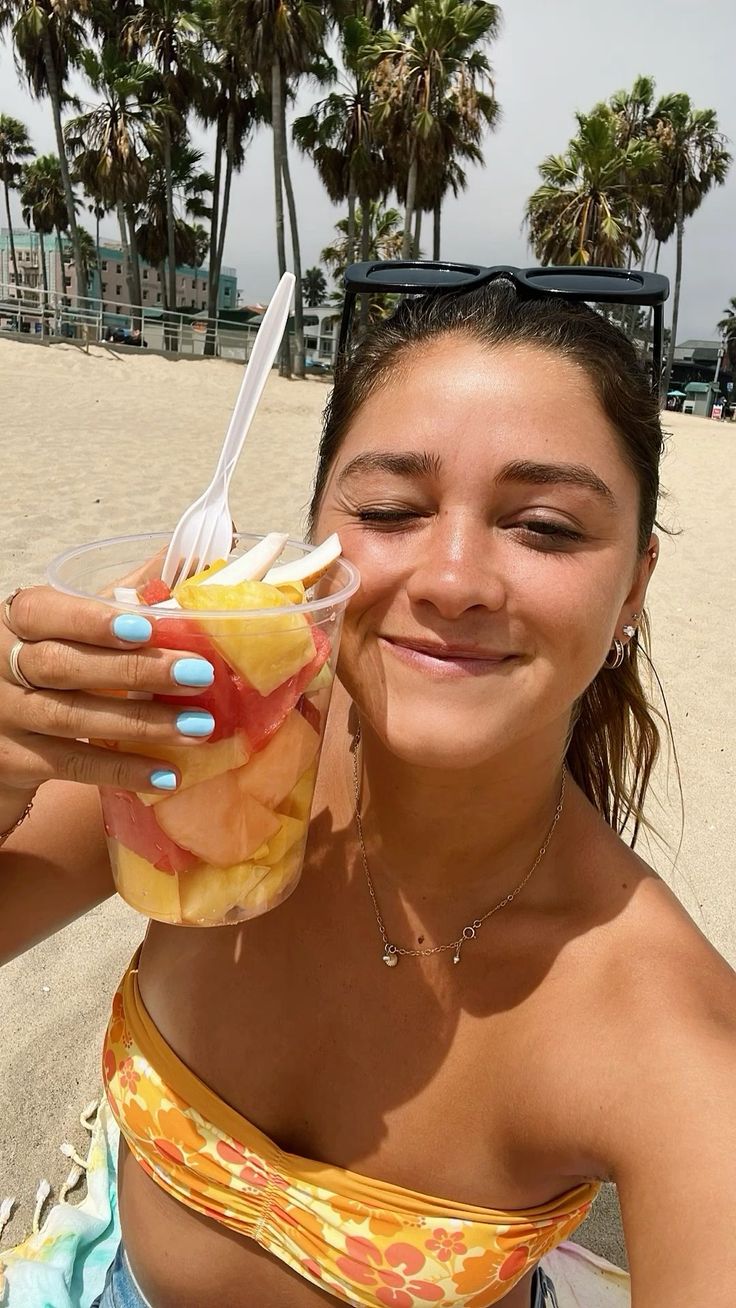 Woman holding a fruit cup on a beach with palm trees in the background