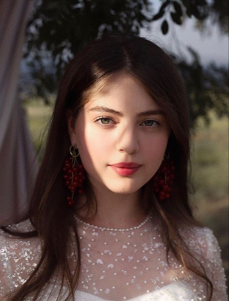 Young woman with long hair and red berry earrings in soft outdoor lighting